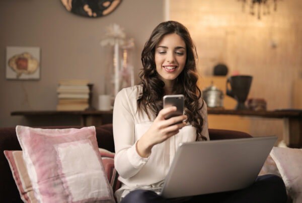 Woman smiling holding her phone sitting in front of her laptop