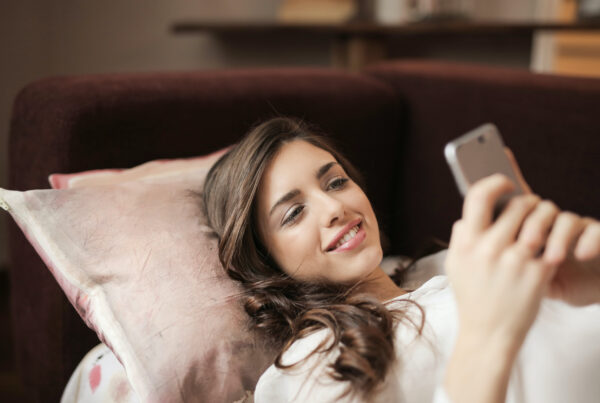Women looking at her phone smiling, laying on the couch
