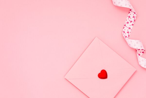 pink background, pink envelope sealed with red heart, pink ribbon