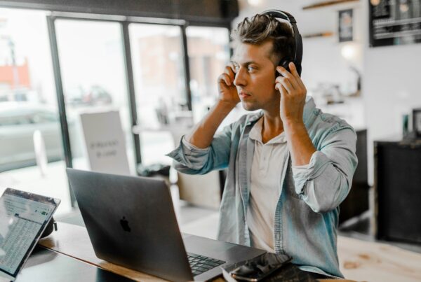 Employee sitting on his MacBook in a modern looking office putting on headphones